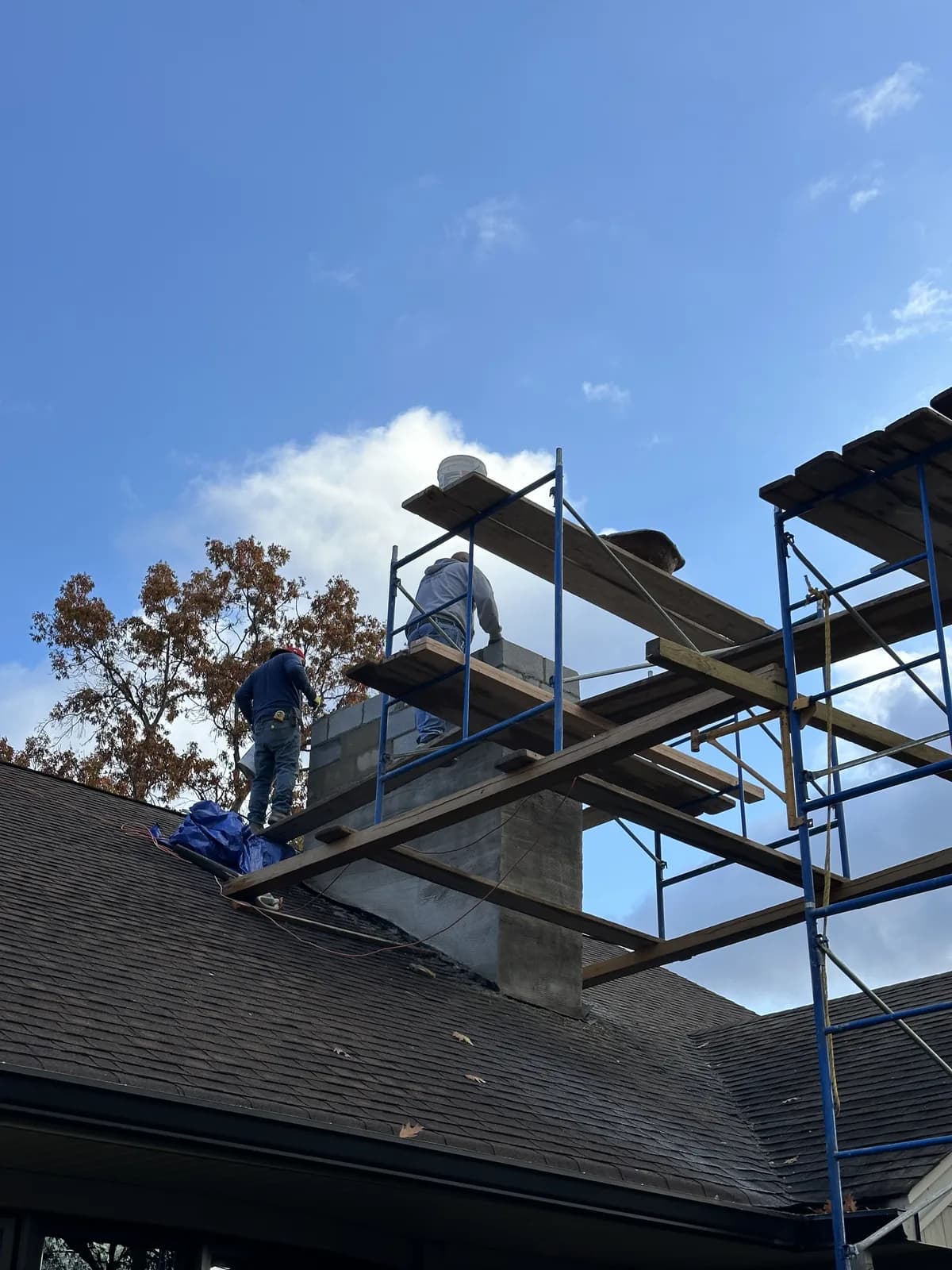 Crew rebuilding a chimney from scaffolding above a NJ roofline